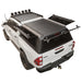 A white Toyota Hilar pickup truck shown from a rear three-quarter angle, fitted with a black hardtop canopy over the bed, and a rear window opening. The product appears to be the truck canopy/accessory.